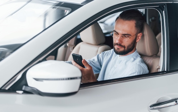 Zijaanzicht van een jonge knappe man in formele kleding die in een gloednieuwe auto zit