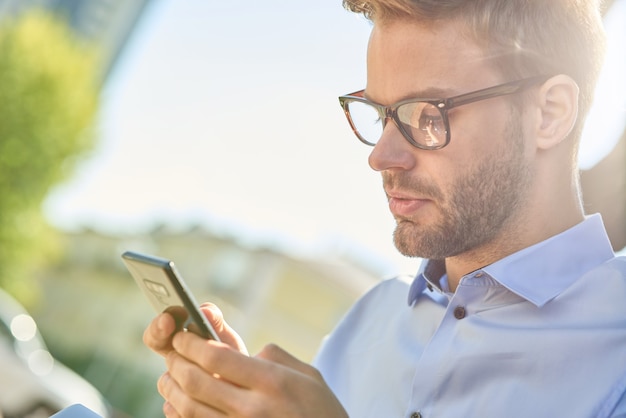 Zijaanzicht van een jonge knappe zakenman die smartphone gebruikt terwijl hij buiten op de bank zit op een