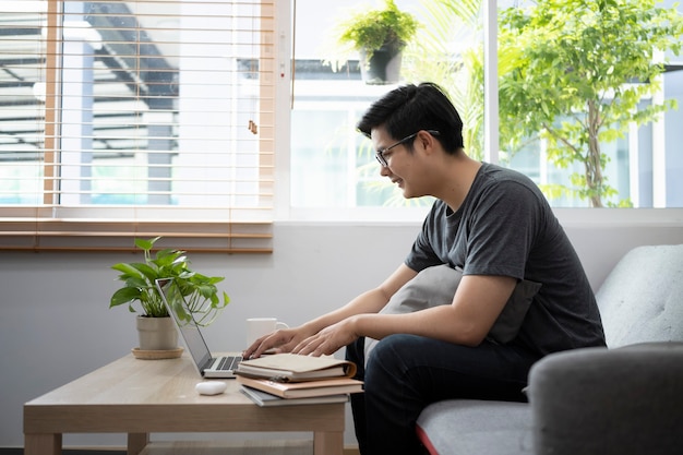 Zijaanzicht van een jonge man die online werkt met een computerlaptop in de woonkamer.