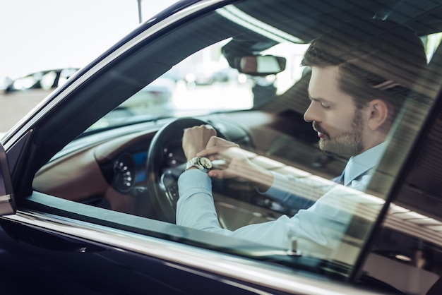 Zijaanzicht van een jonge zakenman die de tijd controleert op polshorloges die in de auto zitten