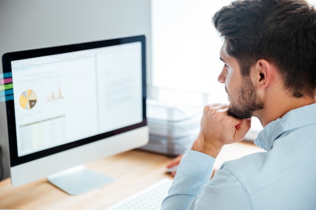 Zijaanzicht van een jonge zelfverzekerde knappe zakenman die op een laptop op kantoor werkt