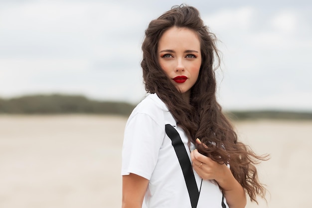 Zijaanzicht van een kalme vrouw met rode lippen en lang golvend haar die tijdens een bewolkte dag aan de kust staat