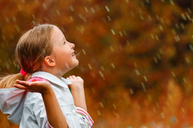 Zijaanzicht van een klein meisje dat zich in de herfstpark bevindt in de regen.