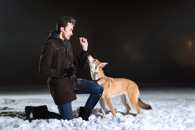 Foto zijaanzicht van een man met een hond van gemengd ras 's nachts buiten in de winter