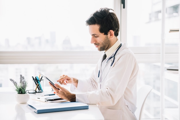 Foto zijaanzicht van een mannelijke arts die digitale tablet in kliniek gebruiken