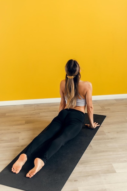 Zijaanzicht van een mooie jonge vrouw in sportkleding die yoga beoefent op een oefenmat op een gele achtergrond Stretching van de spieren van de rug en benen yoga