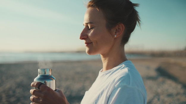 Zijaanzicht van een mooie vrouw die water drinkt en geniet van yoga in de ochtend op het strand Sportief meisje dat er na de training gelukkig uitziet aan de zee te rusten