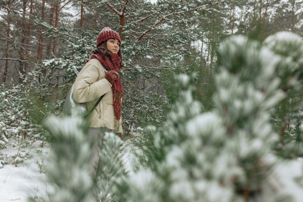Zijaanzicht van een reizende vrouw die met rugzak in het besneeuwde winterbos loopt met naaldbomen