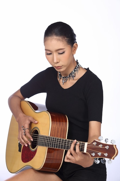 Zijaanzicht van een vrouw met een bruine huid die een klassieke gitaar vasthoudt en kalm speelt, ontspant. Concept van kunst en creativiteit, studio verlichting witte achtergrond, kijk naar de hand