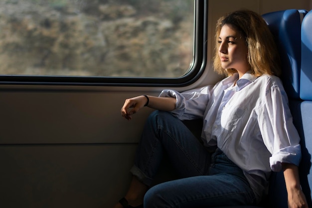 Zijaanzicht van een vrouw met een oosterse uitstraling in een wit overhemd en een spijkerbroek zit in een trein