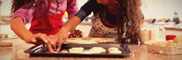 Zijaanzicht van een vrouw van gemengd ras in een keuken met haar jonge dochter met Kerstmis, koekjes maken en elkaar aankijken