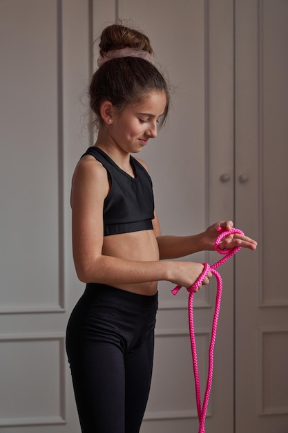 Zijaanzicht van fit gerichte preteen gymnast in zwarte top en legging met haarknotje staande in de kamer en voorbereiden op touwtjespringen thuis