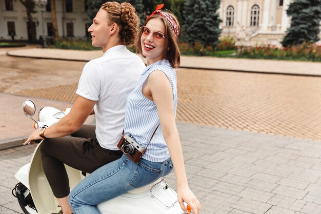 Zijaanzicht van gelukkige jonge mooie paar samen rijden op scooter buitenshuis