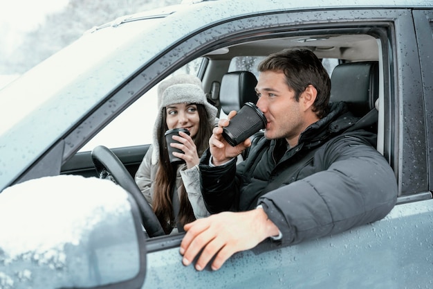 Zijaanzicht van het paar dat tijdens een roadtrip geniet van een warm drankje in de auto