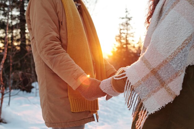 Zijaanzicht van jonge aanhankelijke en amoureuze dates in winterkleding die voor elkaar staan en bij de hand in het bos vasthouden tijdens het winterweekend