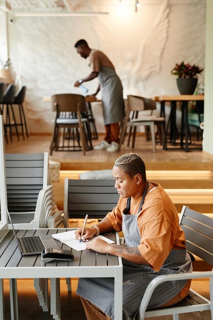 Zijaanzicht van jonge man en vrouw die in een modern café werken en meubels voorbereiden en aantekeningen maken voordat ze worden geopend