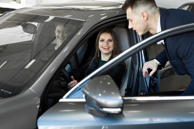 Zijaanzicht van jonge mooie vrouw die in de auto zit en hand op het stuur houdt