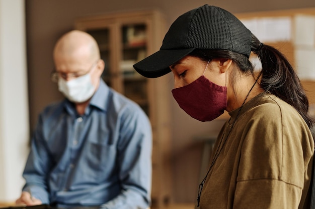 Zijaanzicht van jonge overstuur vrouw met beschermend masker en baseballcap