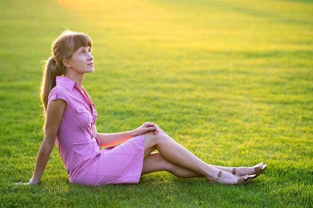 Zijaanzicht van jonge schattige vrouw zittend op het gras bij mooi weer. Concept van rusten op frisse lucht op de natuur.