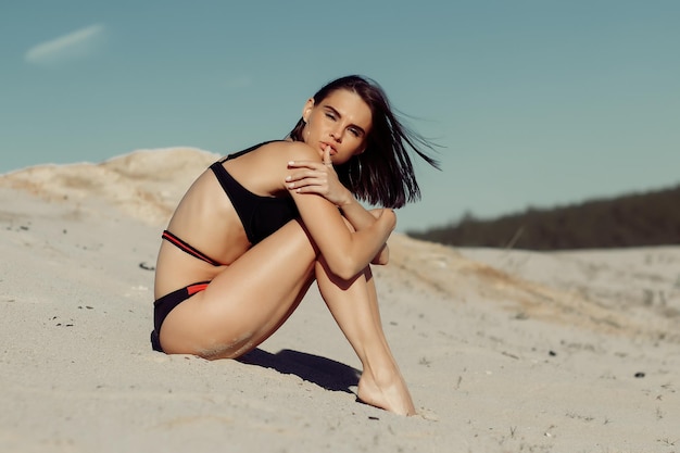 Zijaanzicht van jonge vrouw in sierzwempak zittend op zandheuvel op zonnige dag op het strand