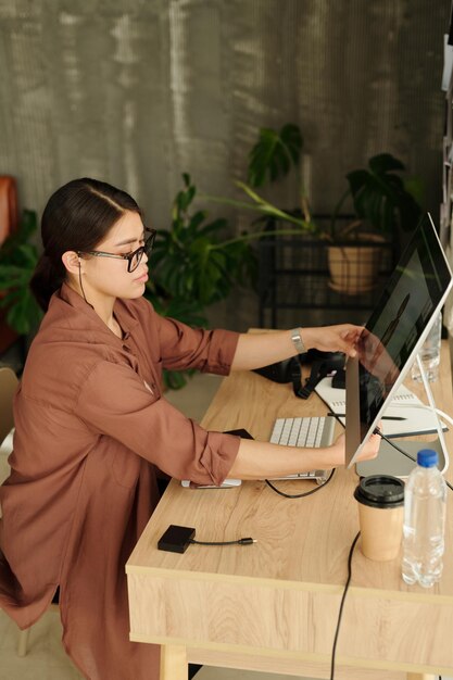 Zijaanzicht van jonge vrouwelijke fotograaf die computermonitor aanpast