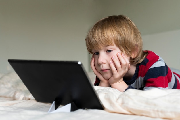 Foto zijaanzicht van jongen die tablet in bed gebruikt