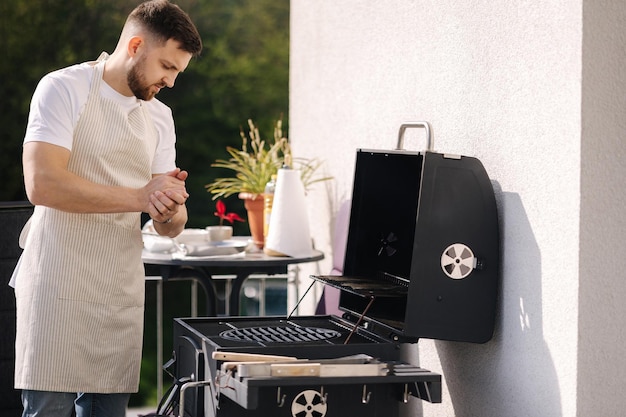 Zijaanzicht van knappe man, probeer hoe heet bbq-grill is, man in schort maakt diner buiten