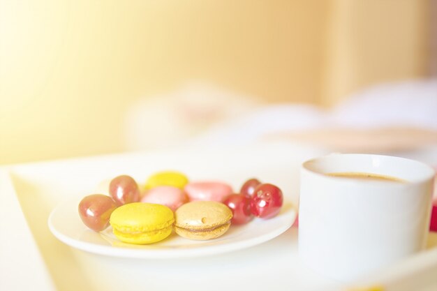 Zijaanzicht van kop koffie met smakelijke kleurrijke macarons of bitterkoekjes op wit dienblad