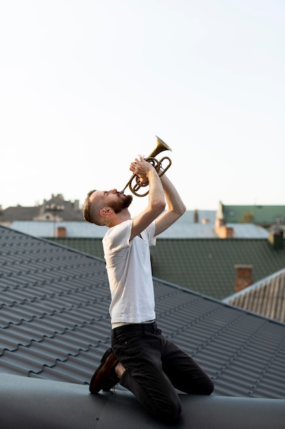 Zijaanzicht van mannelijke artiest die de cornet op het dak speelt