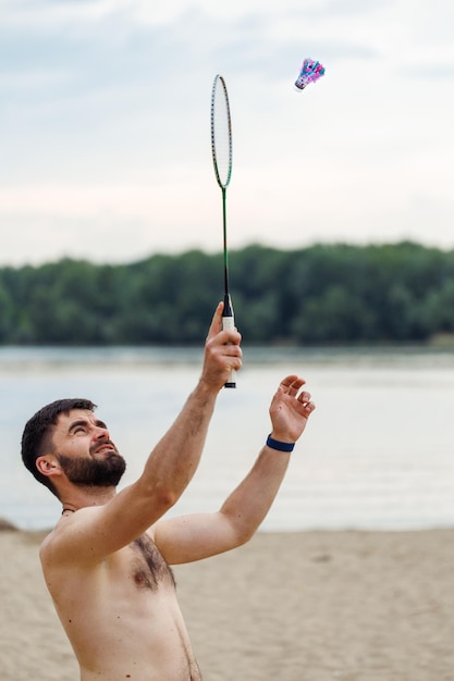 Zijaanzicht van middelbare leeftijd bebaarde shirtless naakte man met kort donker haar badminton spelen op hemelachtergrond Summer