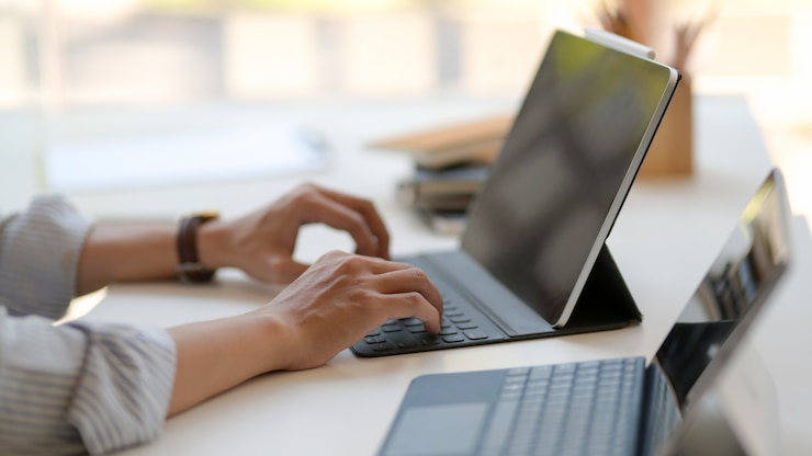 Foto zijaanzicht van ondernemer die aan digitale tabletten op witte lijst in moderne werkplaats werkt