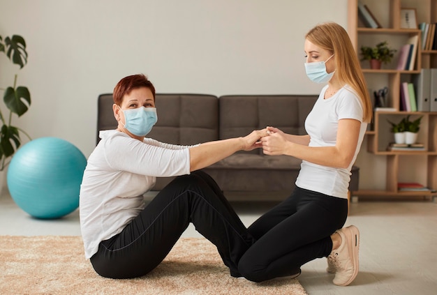 Foto zijaanzicht van oudere vrouw met medisch masker in covidherstel die fysieke oefeningen doet