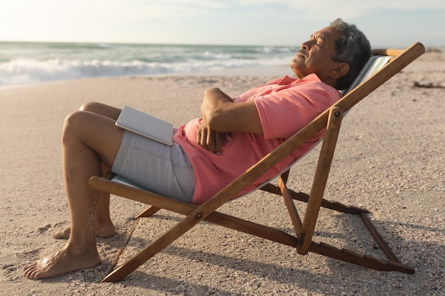 Zijaanzicht van senior biracial man met laptop slapen op klapstoel ontspannen op het strand