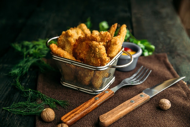 Zijaanzicht van smakelijke gebakken kipnuggets in metalen manden op een houten tafel