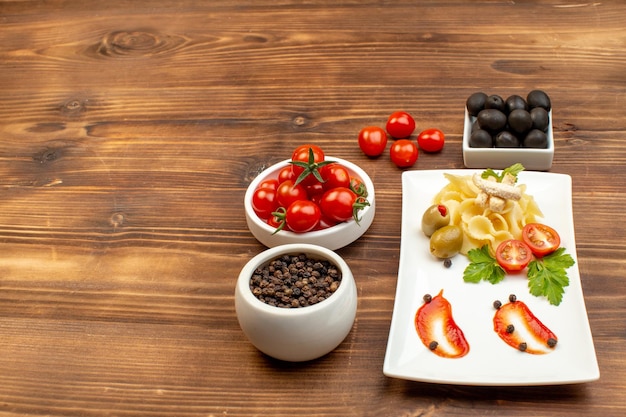 Zijaanzicht van smakelijke pastamaaltijd geserveerd met groenten op een witte plaat, tomaten, olijven, peper op bruin houten oppervlak