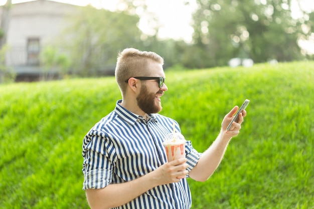 Zijaanzicht van stijlvolle jongeman met bril en een baard met een milkshake die op video praat met zijn
