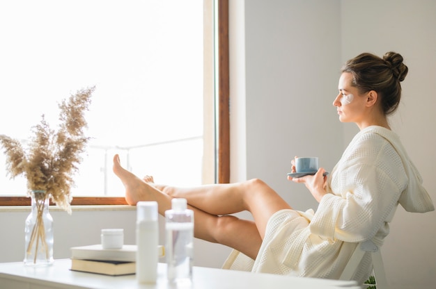 Zijaanzicht van vrouw die kuuroord van dag thuis genieten terwijl het hebben van koffie