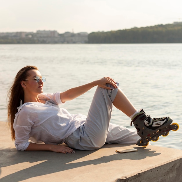 Foto zijaanzicht van vrouw met rolschaatsen poseren in de zon aan het meer