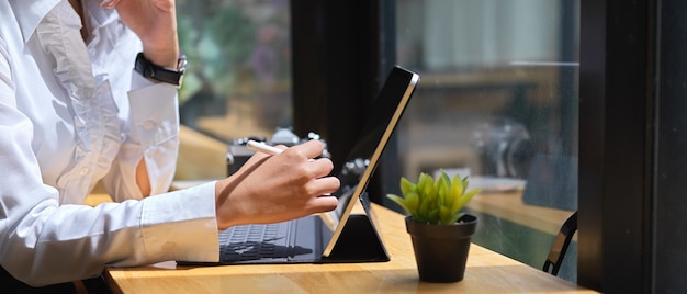 Zijaanzicht van vrouwelijke hand met behulp van digitale tablet met stylus-pen op houten tafel