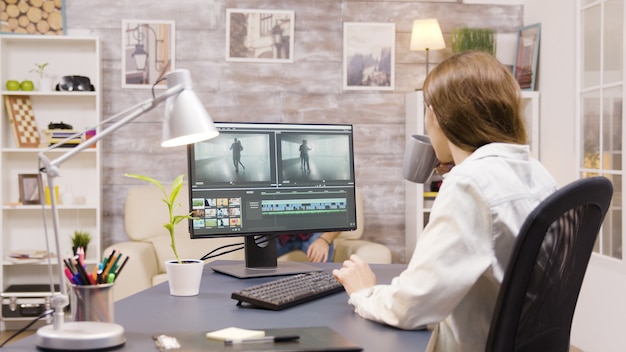 Zijaanzicht van vrouwelijke videograaf die werkt aan de postproductie van een film vanuit huis. Vriend op de achtergrond.