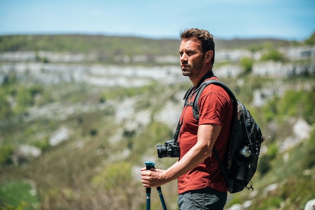 Zijaanzicht van wandelaar met trekkingstokken met rugzak en fotocamera die landschap observeert