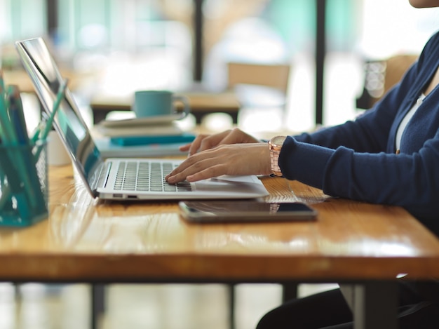 Zijaanzicht van zakenvrouw handen typen op laptop toetsenbord op houten tafel met smartphone en briefpapier