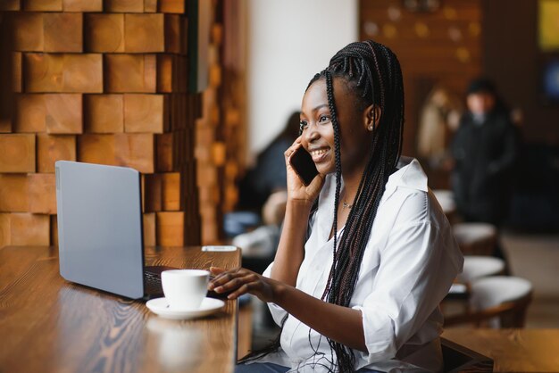 Zijaanzicht van zwarte dame die van koffie in de ochtend geniet en e-mails controleert op laptop, café-interieur, lege ruimte