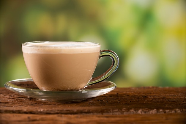 Foto zijaanzicht warme koffie (cappuccino latte mokka) in helder glas op houten tafel in zonnige, kopieer ruimte.