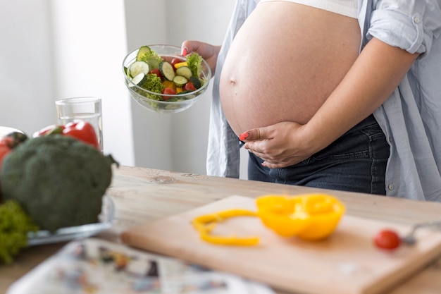 Foto zijaanzicht zwangere vrouw die een salade houdt