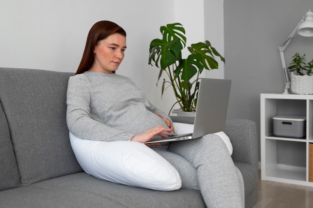 Foto zijaanzicht zwangere vrouw met laptop thuis