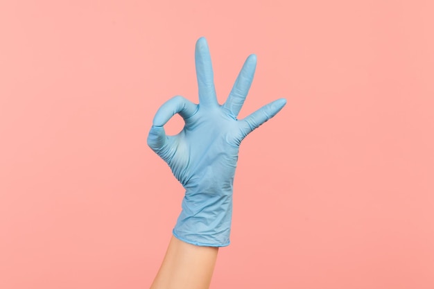 Zijaanzichtclose-up van menselijke hand in blauwe chirurgische handschoenen die Ok teken of nummer 3 met vingers tonen.