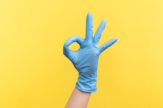Zijaanzichtclose-up van menselijke hand in blauwe chirurgische handschoenen die Ok teken of nummer 3 met vingers tonen.