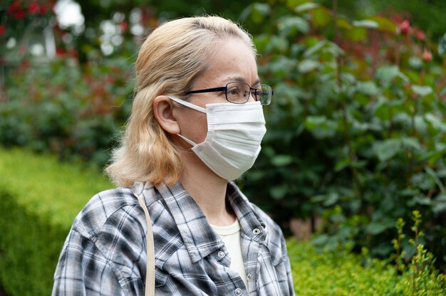 Zijaanzichtportret van blonde vrouw van middelbare leeftijd met oogglazen die wit chirurgisch masker dragen. Bescherming tegen Coronavirus (COVID-19)