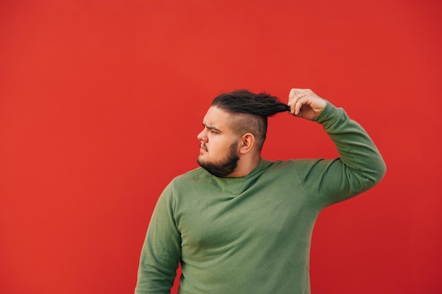 Zijaanzichtportret van een knappe man met overgewicht in een groen sweatshirt op een rode achtergrond